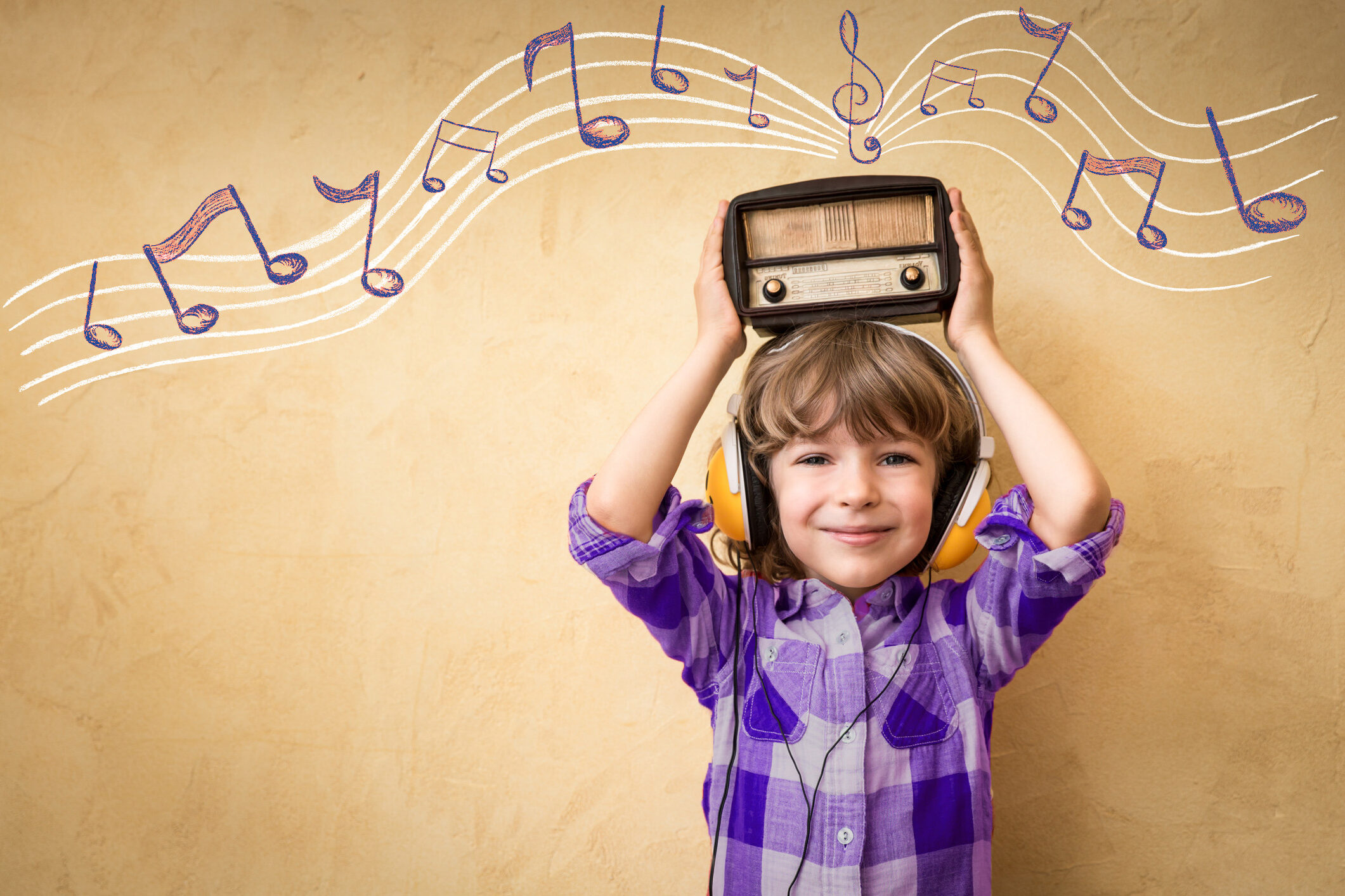 Little boy holding up a retro style radio over his head. in the background there are crayon-drawn musical notes.